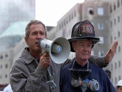 NEW YORK, NY - SEPTEMBER 14: US President George W. Bush (L), standing next to retired firefighter Bob Beckwith, 69, speaks to volunteers and firemen as he surveys the damage at the site of the World Trade Center in New York in this 14 September 2001 file photo. Bush was presented with the same bullhorn he used to address the rescue workers in this photo at a ceremony 25 February 2002 in the Oval Office of the White House in Washington, DC which was attended by Beckwith and New York Governor George Pataki. The President said the bullhorn would be put on display at his father's Presidential Library. (Photo credit should read PAUL RICHARDS/AFP/Getty Images)